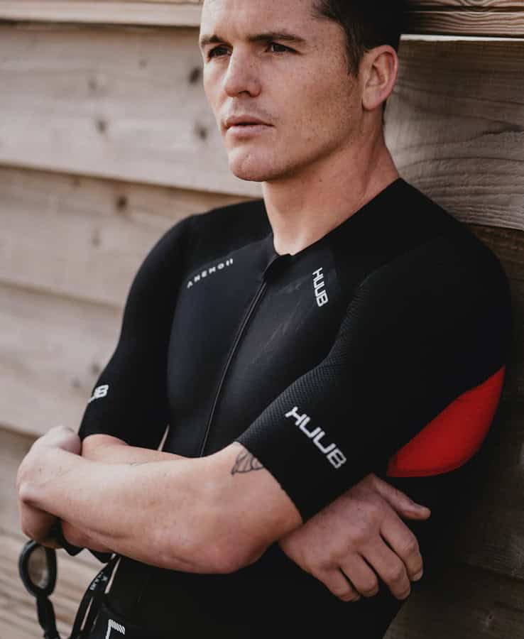 Triathlon training athlete wearing HUGO sports gear, close-up portrait, focused and determined, against wooden background, promoting triathlon performance and endurance.