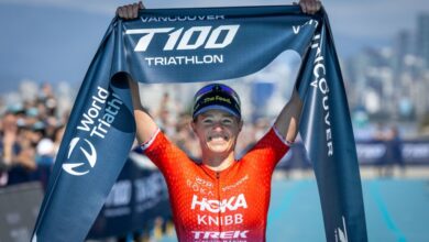 Triathlon athlete celebrating Victory at Vancouver T100 Triathlon, holding the finish line tape, with a crowded background and city skyline, showcasing triumph in endurance sport.