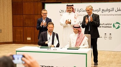 Sponsorship agreement signing at a triathlon event in Saudi Arabia, with officials and representatives celebrating the partnership in a formal setting.