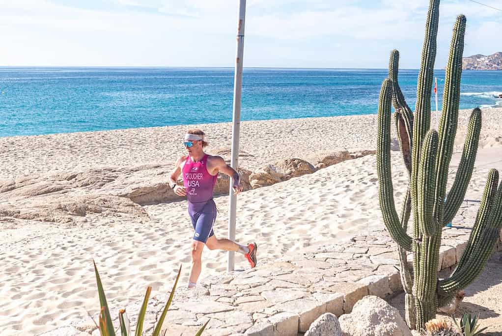 1. Female triathlete running along a sandy beach during competition, Ocean background, sunny weather, sports gear, focus on endurance and outdoor training.