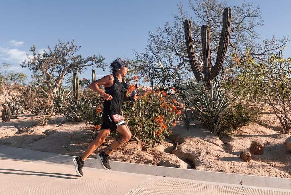 A female triathlete running through a desert landscape with cacti and desert plants, demonstrating endurance training in arid conditions for triathlon preparation and outdoor sports performance.