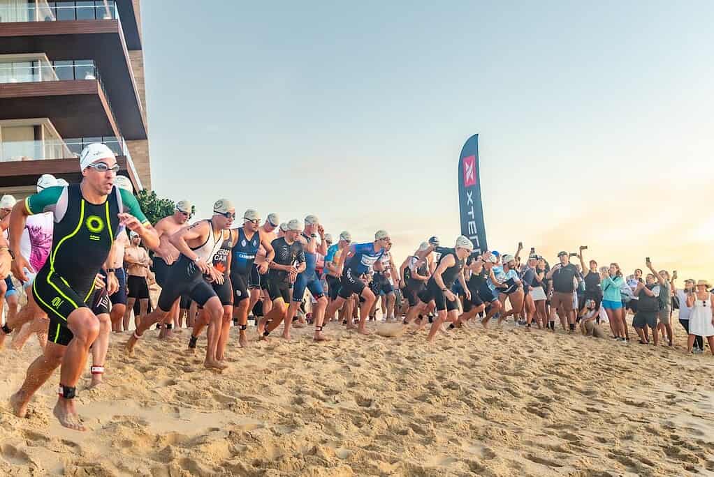 High-performance triathletes start the swim segment at a competitive triathlon event on a sandy beach, showcasing endurance and sprinting skills typical in triathlon training and competition.