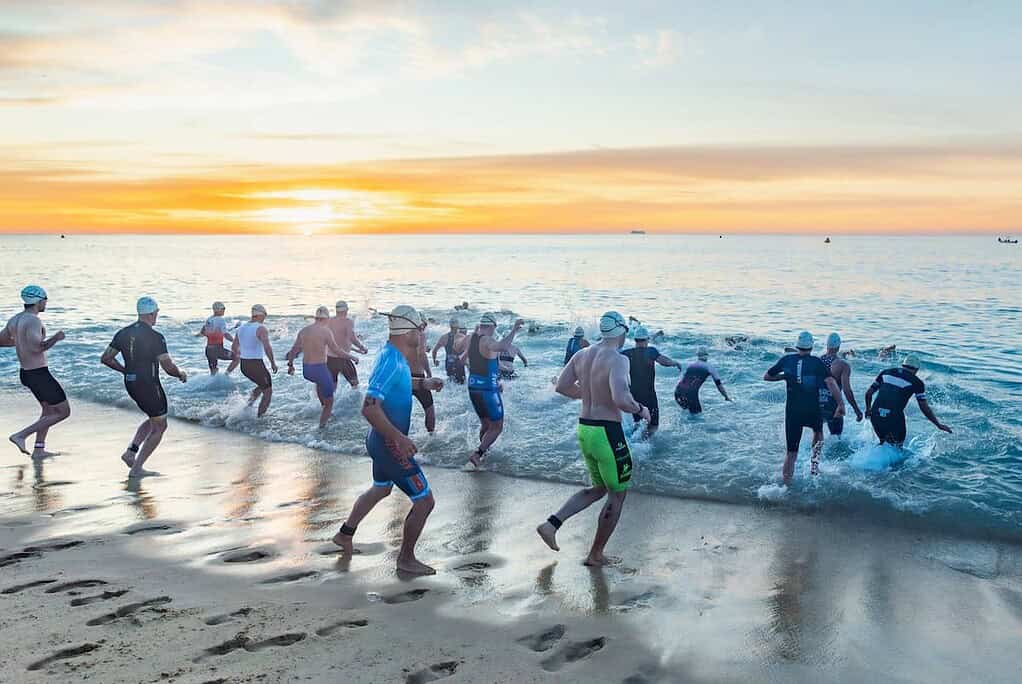 Swimmers entering the sea at a triathlon event during sunrise, showcasing endurance training and open water swimming for triathletes.