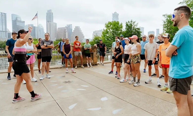 Active triathlon training session outdoors with a coach instructing diverse group of athletes, city skyline in background, focusing on triathlon preparation and fitness motivation.