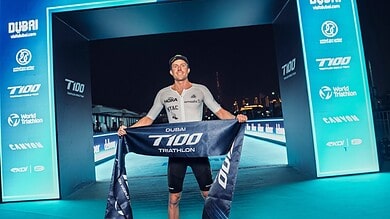 Competitive triathlete crossing the finish line at Dubai T100 Triathlon event, celebrating success with backdrop of the marathon arch and night skyline, highlighting endurance and triathlon achievements.