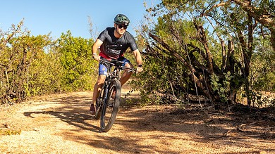 Adventurous cyclist riding mountain bike through rugged trail in natural outdoor setting with blue sky, perfect for triathlon training and endurance sports.
