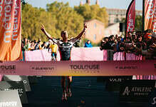 Endurance triathlon athlete crossing finish line with victory celebration, surrounded by cheering spectators at Toulouse triathlon event, showcasing athletic achievement, competitive sports and endurance.
