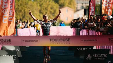 Endurance triathlon athlete crossing finish line with victory celebration, surrounded by cheering spectators at Toulouse triathlon event, showcasing athletic achievement, competitive sports and endurance.