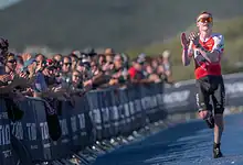 Sam Dickinson running towards the finish line at the Singapore T100 Triathlon, with spectators cheering in the background.