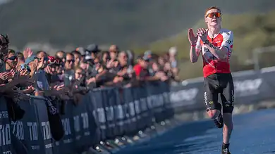 Sam Dickinson running towards the finish line at the Singapore T100 Triathlon, with spectators cheering in the background.