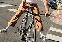 Dynamic urban cyclist balancing on a bike in a city environment with modern buildings and clear blue sky.