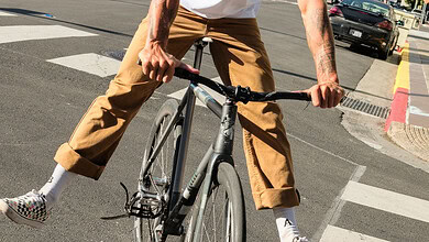 Dynamic urban cyclist balancing on a bike in a city environment with modern buildings and clear blue sky.