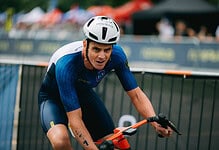 Male triathlon athlete in blue cycling gear and helmet riding a bike during a race, demonstrating endurance and focus at a competitive triathlon event.