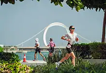 Female triathlete running along a scenic waterfront course during a triathlon event.