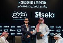 Two men shaking hands during the MOU signing ceremony for triathlon collaboration, with a backdrop displaying logos of PTO and Sela.