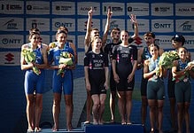 Triathlon athletes on the podium celebrating with medals and flowers at a major event, showcasing athletic achievement and sportsmanship.