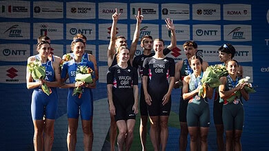 Triathlon athletes on the podium celebrating with medals and flowers at a major event, showcasing athletic achievement and sportsmanship.