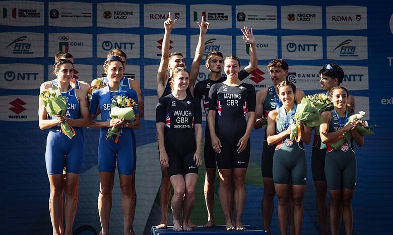 Triathlon athletes on the podium celebrating with medals and flowers at a major event, showcasing athletic achievement and sportsmanship.