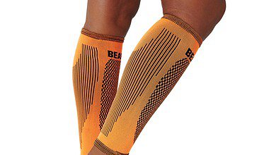 Orange compression leg sleeves on a runner's legs, showing athletic branding and patterns for tight fit and muscle support.