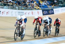 Competitive track cycling race with four athletes in aerodynamic positions on velodrome bikes during a triathlon event.