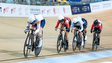 Competitive track cycling race with four athletes in aerodynamic positions on velodrome bikes during a triathlon event.