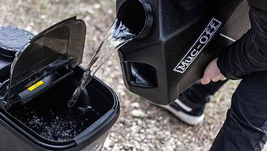 Water being poured from a Muc-Off tank into a mobile pressure washer