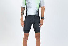 Male triathlete in cycling gear with sunglasses, standing against a white background, showcasing professional triathlon apparel and equipment.