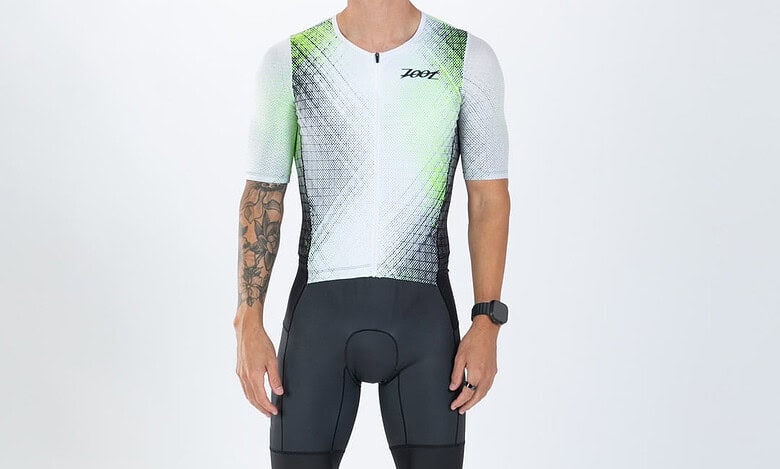 Male triathlete in cycling gear with sunglasses, standing against a white background, showcasing professional triathlon apparel and equipment.