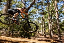 Mountain biker in mid-air jump through forest trail during a mountain biking event, showcasing skill and adventure in outdoor terrain.